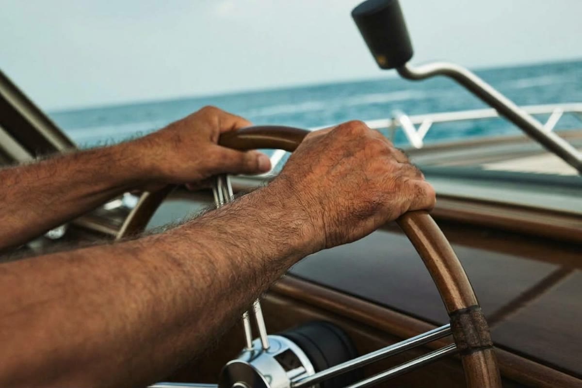 A captain’s hands on the wheel of a motor yacht, with the sea on the horizon
